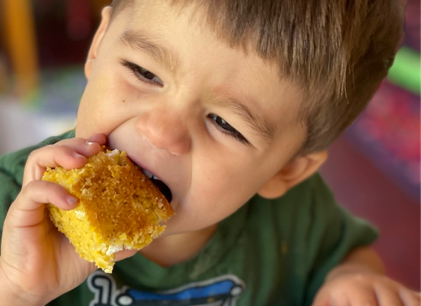 Toddler biting square of corn bread