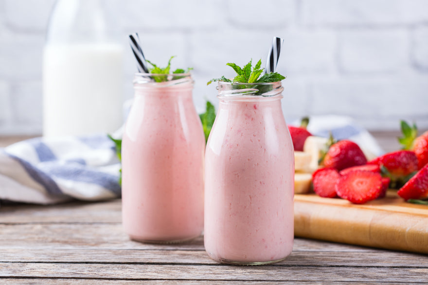 Two jars of strawberry smoothie on a kitchen table.