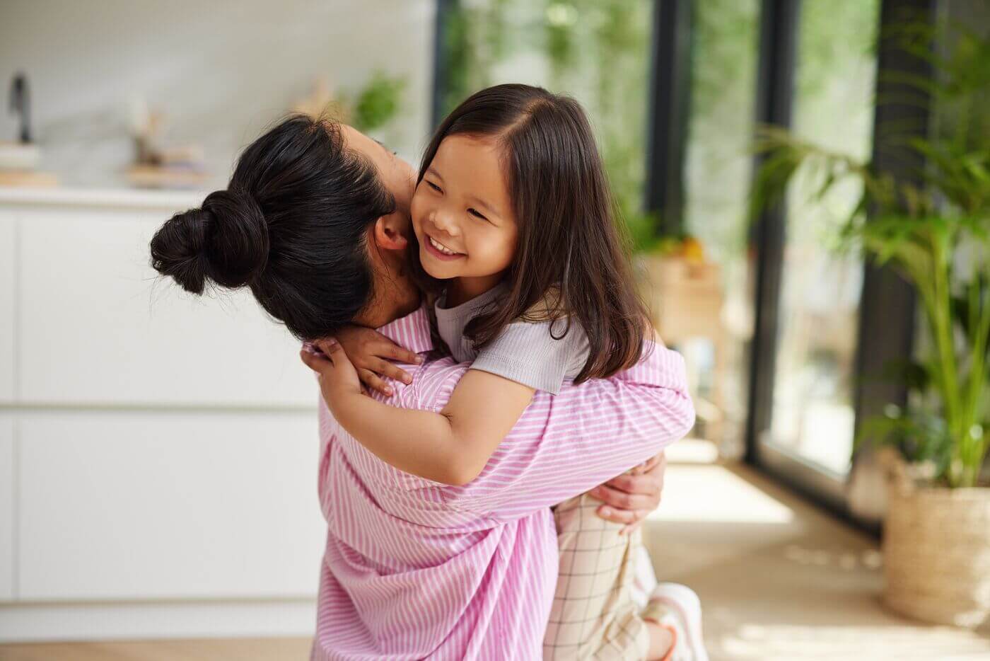 Mom in pink shirt and bun in hair holding her smiling child