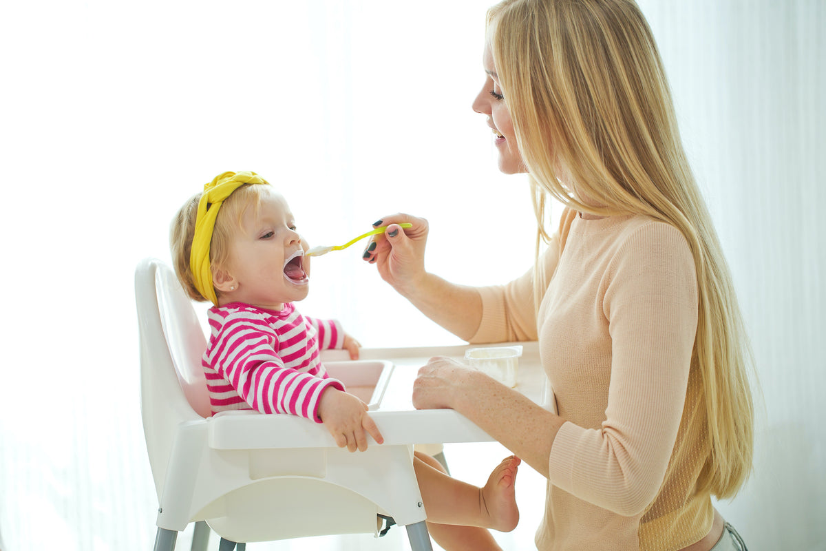 Caucasian mom feeding toddler in high chair
