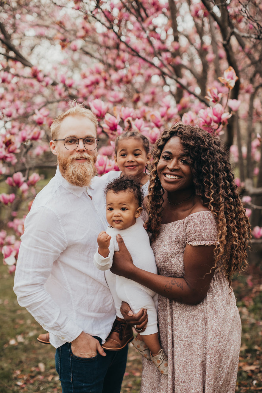 Happy family of four outside by a cherry blossom tree in the Spring