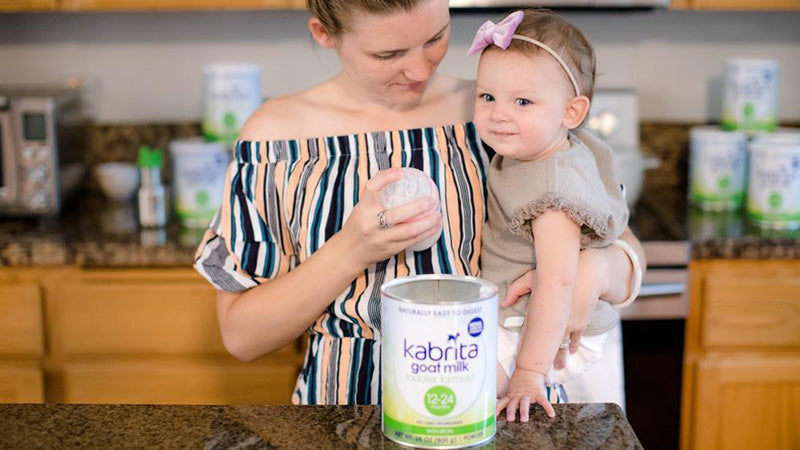 Mom holding baby while making a bottle with Kabrita