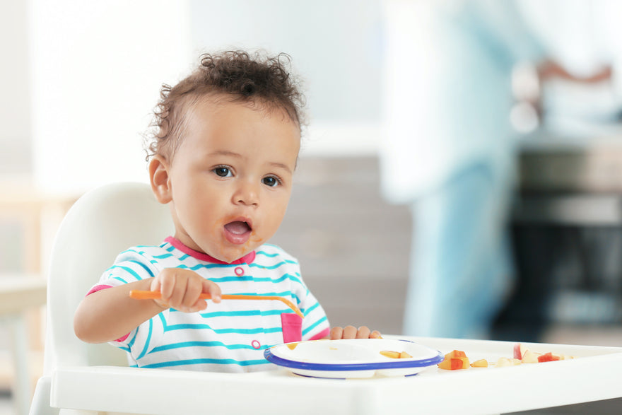 Toddler eating fruits with a spoon from highchair