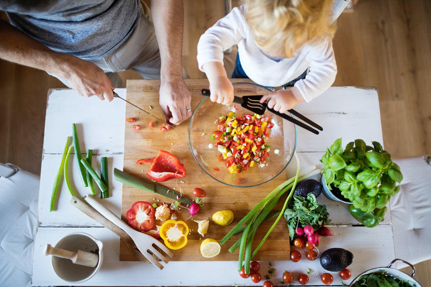 Young father preparing vegetables with toddler boy in kitchen