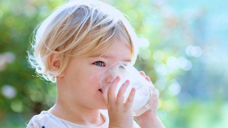 Blond curly-haired toddler drinking milk from a glass