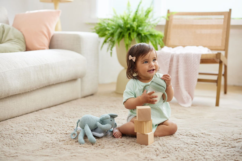 Child sitting on floor drinking from a sippy cup and playing with blocks