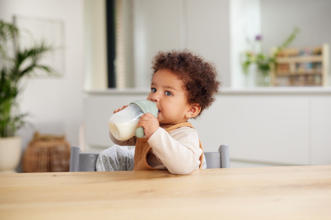 Child with yellow overalls drinking from a sippy cup