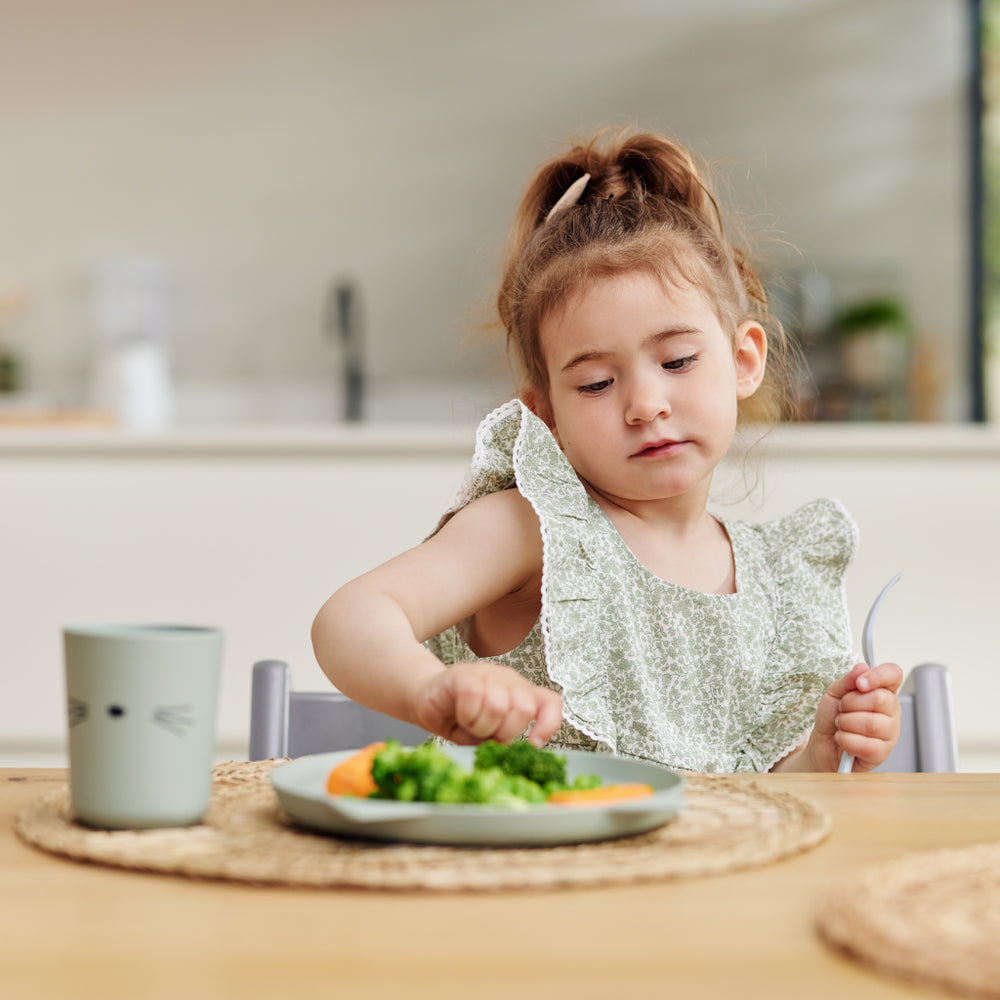 Young girl sitting at breakfast table pushing plate of vegetables away 